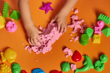 Naklejka na ściany i meble The hands of a child playing with kinetic sand. Close up. Orange background