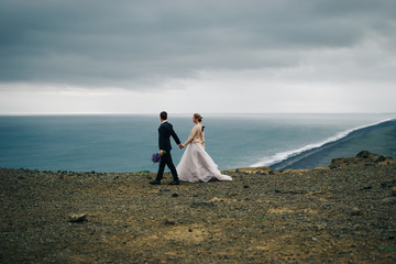 Young wedding couple walking outdoors on background of mountain landscape and ocean with black beach - 243046131