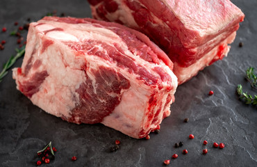 large raw pieces of pork ribs for BBQ on dark stone background, close-up