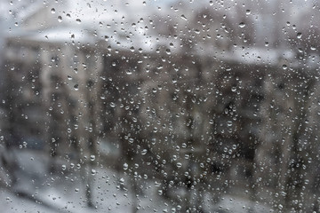 View of the city in a snowfall through a window covered with water drops.