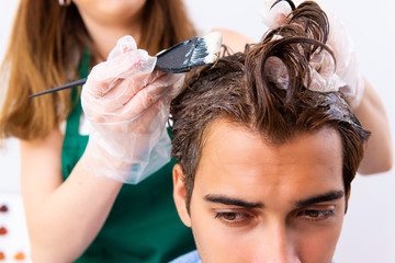 Fototapeta premium Woman hairdresser applying dye to man hair