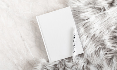 Fuzzy white fur plaid and and white notebook on marble table. Flat lay, top view, copy space