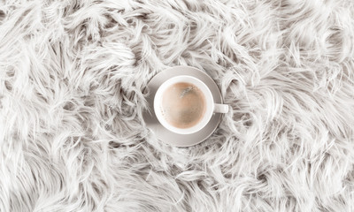 Fuzzy white fur carpet and cup coffee. Fluffy fake textile fur. Flat lay, top view, copy space 