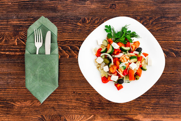 Greek salad of fresh cucumber, tomato, sweet pepper, lettuce, red onion, feta cheese and olives with olive oil. Healthy food, top view with appliances