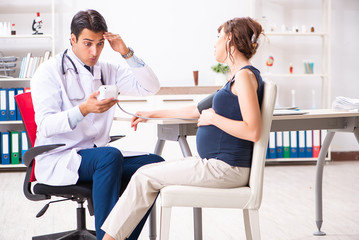 Fototapeta premium Young doctor checking pregnant woman's blood pressure