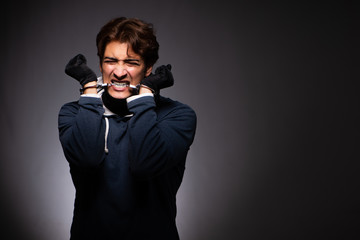 Young gangster in hood on grey background 