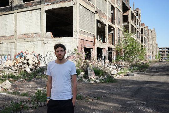 Attractive young man standing outdoor in front of abandoned house, looking at camera. Photo taken in Detroit, Michigan, USA.