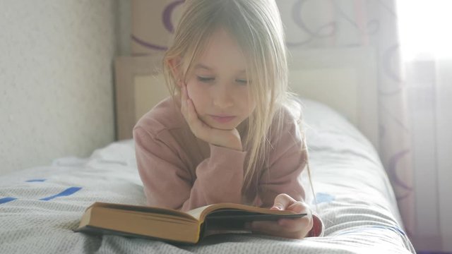 Girl child lay bed read book. Girl kid long hair cute pajamas relax and read fairytale book. Pleasant time in cozy bedroom.