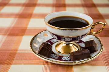 Vintage cup of coffee with chocolate candies on a checkered tablecloth.