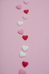 Flatlay with tiny heart-shaped sugar sprinkles in red, white and pink laid out in trace of trail as card for Valentine's Day on February 14th on wooden background, symbol of love and romantic feeling