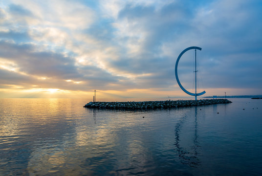 Lausanne, Switzerland - DECEMBER 2018: Dramatic tranquil silhouette beautiful sunset at Geneva lake with scenery of embankment Eole Sculptural landmark and background of pier in Lausanne, Switzerland.