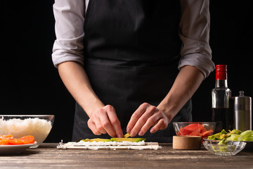 A woman makes Japanese sushi rolls at home. Japanese food, and a recipe book menu.