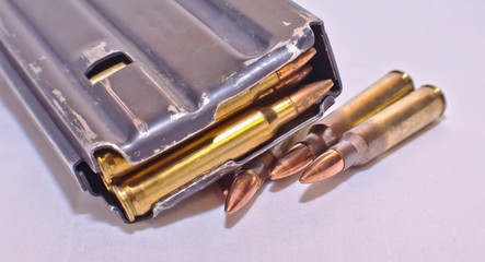 A loaded AR-15 rifle magazine on top of four .223 caliber bullets on a white background