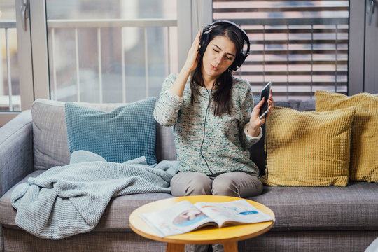 Cheerful woman listening to music with large headphones and singing.Enjoying listening to music in free time at home.Relaxing with music,happy woman singing.Positive mood.