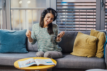 Cheerful woman listening to music with large headphones and singing.Enjoying listening to music in free time at home.Relaxing with music,happy woman singing.Positive mood