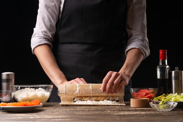 A woman makes Japanese sushi rolls at home. Japanese food, and a recipe book menu.