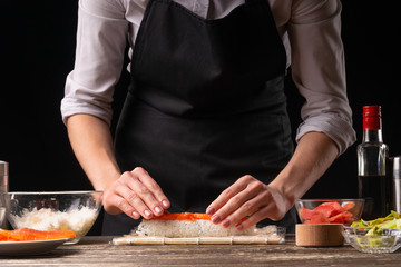 A woman makes Japanese sushi rolls at home. Japanese food, and a recipe book menu.