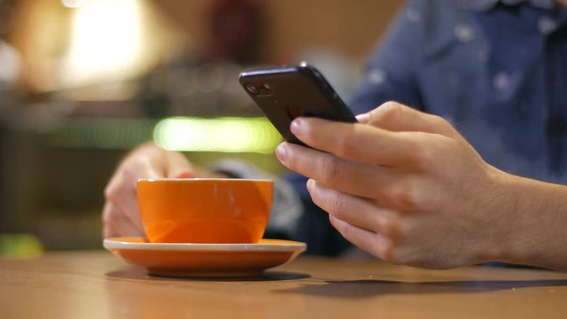 Man using smartphone and drinking from a steaming cup of coffee in a coffee shop. High quality footage 4K ProRes 422 HQ