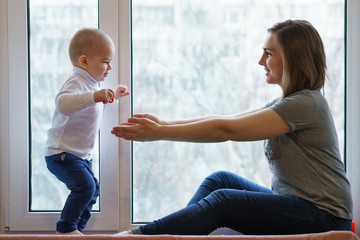 Mother and child are sitting on windowsill. Woman stretches her arms to her son. Winter day outside...