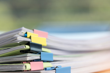 Close up stack of paperwork. Pile of unfinished homework assignment stacked in archive with colorful binder paper clips on table waiting to be managed and inspected. Education and business concept.