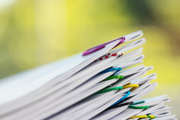 Close up pile of unfinished homework assignment stacked in archive with colorful paper clips on table in school waiting to be managed and inspected. Stack of paperwork. Education and business concept.