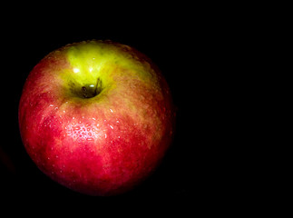Water droplet on glossy surface of red apple on black background