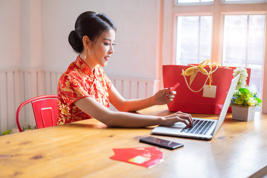 Happy chinese woman wearing a qipao dress traditional and buying online with a red credit card. Online Shopping Website on Laptop.