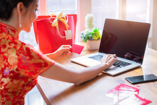 Happy chinese woman wearing a qipao dress traditional or cheongsam holding a red credit card and purchasing online website on black screen laptop mockup for graphic montage. - Powered by Adobe