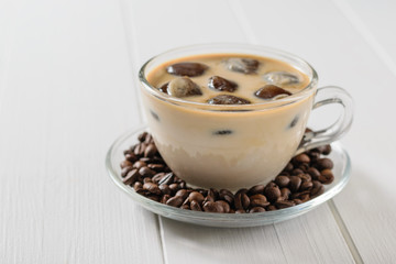 Glass bowl with ice coffee and coffee beans on white wooden table.