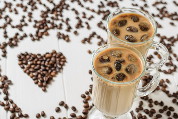 Two glasses with ice coffee and cocktail tubes on the background of the heart of coffee beans.