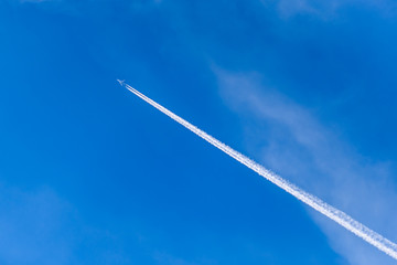 A distant aircraft with long diagonal condensation trails or contrails on a blue sky day