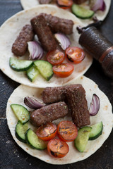 Close-up of tortilla flatbread with bbq balkan cevapi sausages and vegetables, studio shot