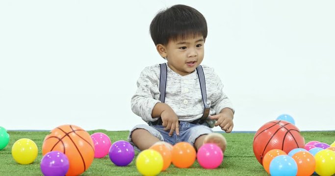 Asian boy playing balls, then he smiling and pitching ball, many balls beside him, concept for Asian boy playing balls alone.