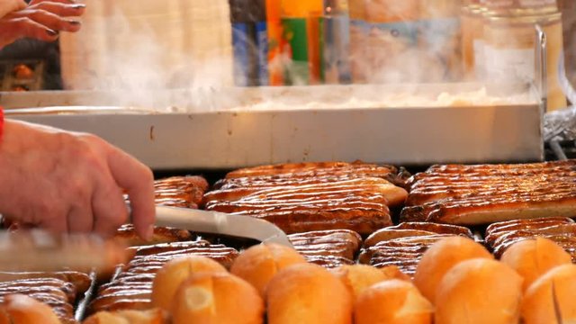 Christmas market, national German sausages are grilled, next to buns. Women's hands turn Nuremberg sausages with help of special tweezers