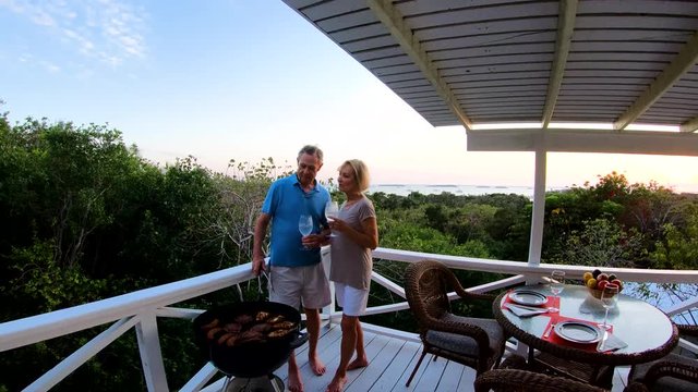 Senior couple grilling on terrace at sunset Bahamas 