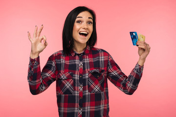 Cheerful happy surprised young woman with credit card showing sing ok over pink background