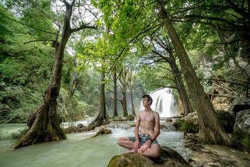 Young Shirtless Man Meditating at Peaceful Waterfall
