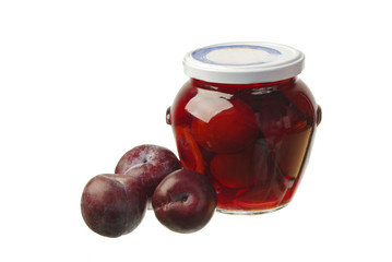 Fresh plums and plum compote in a glass jar.