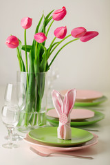 Happy easter. Decor and table setting of the Easter table is a vase with pink tulips and dishes of pink and green color.