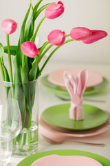 Happy easter. Decor and table setting of the Easter table is a vase with pink tulips and dishes of pink and green color.