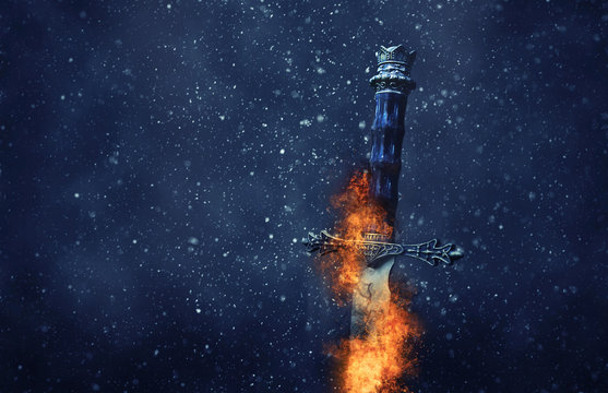 mysterious and magical photo of silver sword with fire flames over gothic snowy black background. Medieval period concept.