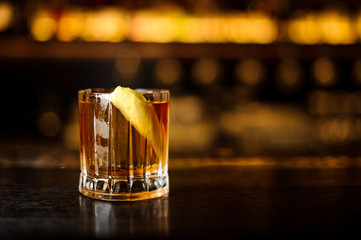 Glass of a Rusty Nail cocktail with orange zest on the wooden bar counter