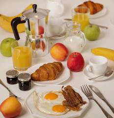 Breakfast time. Fried eggs and bacon. Croissants and orange juice, jam. Coffee with cream or milk. Fruits - bananas, red and green apples.
