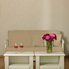 Beige sofa with pillows in the living room and vase with Flowers (Michaelmas daisy, asters), glasses of wine.