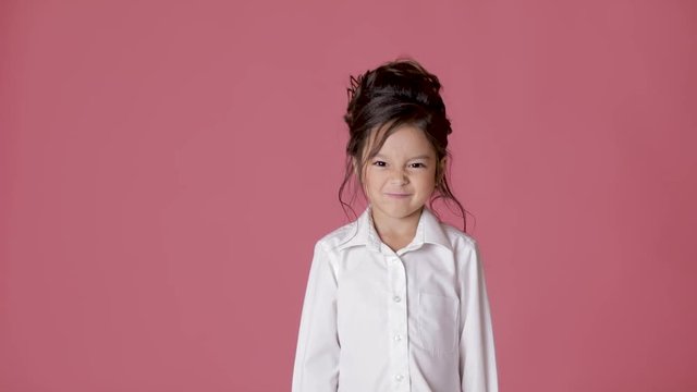 cute little child girl in white shirt shows different emotions on pink background.