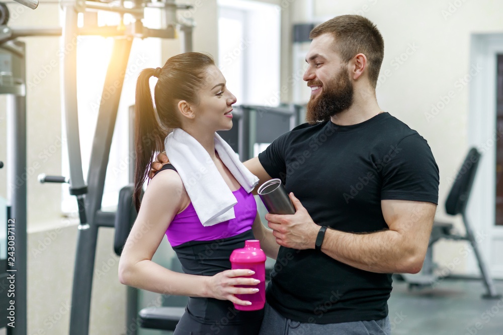 Wall mural Young smiling fitness couple talking in the gym. Sport, training, family and healthy lifestyle