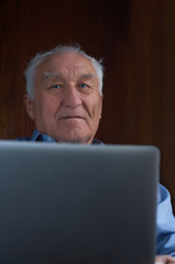 Senior grey-haired man using a laptop sitting in chair at home.