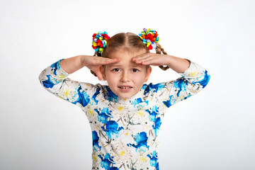 Studio waist up portrait of a little girl wearing shirt with a print and with two pigtails and color bows on a gray background.