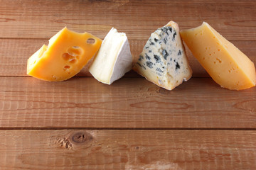 Different types of cheeses on wooden boards. Camembert, hard yellow cheese, dorblu on wooden boards. Copy space