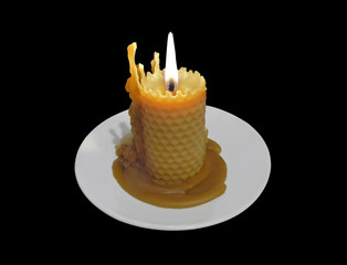 Burning beeswax candle on a white saucer isolated on black background